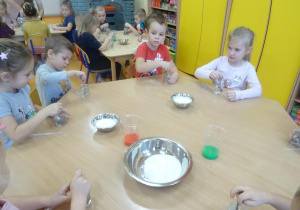 Czwórka dzieci siedzi przy stoliku, w ręku trzymają łyżeczki, którymi mieszają w słoiczkach.